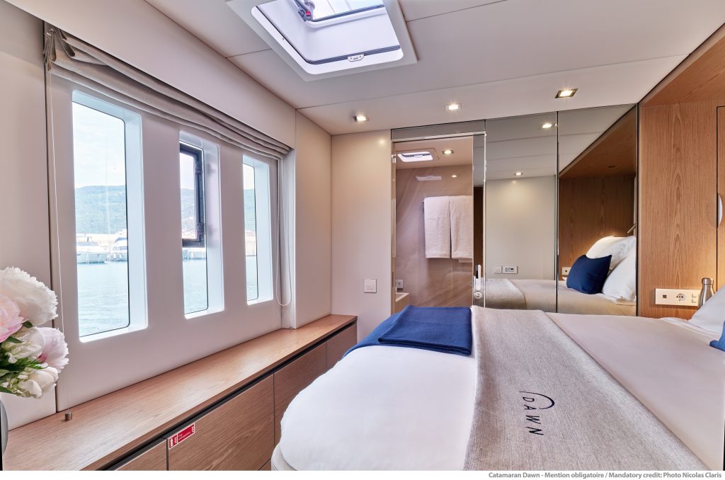 Wnętrze kabiny jachtu Sunreef Yachts z łóżkiem i widokiem na wodę przez okna.