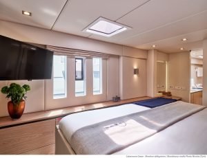Wnętrze luksusowej kabiny na katamaranie Sunreef Yachts z dużym łóżkiem, telewizorem z płaskim ekranem i naturalnym światłem wpadającym przez okna.