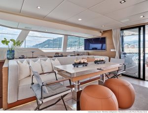 Widok wnętrza katamaranu Sunreef Yachts ukazujący luksusowy salon z jadalnią, dużym telewizorem i eleganckim wyposażeniem z widokiem na port przez duże okna.