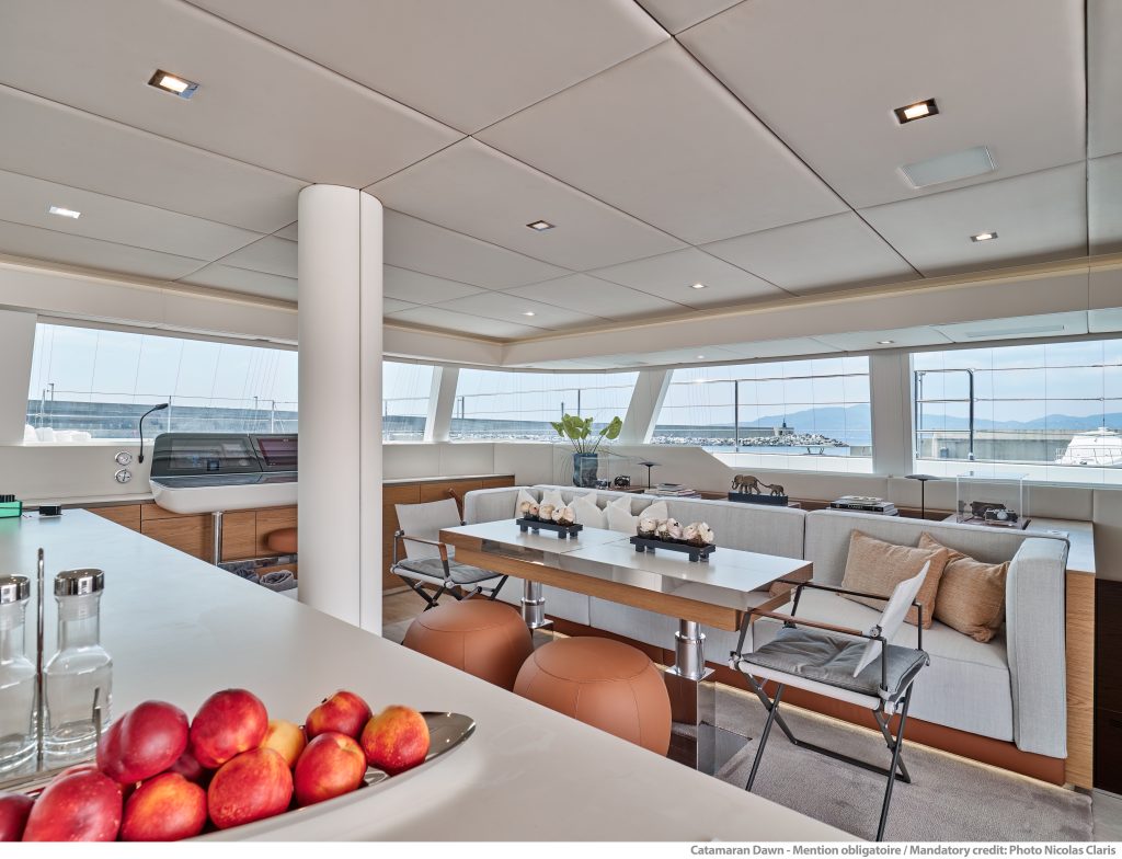Widok wnętrza luksusowego katamaranu Sunreef Yachts ukazujący przestronną jadalnię z dużym stołem, pluszowymi siedzeniami i panoramicznymi oknami.