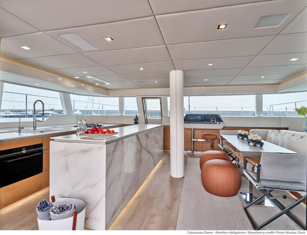 Widok wnętrza luksusowej kabiny Sunreef Yachts z miejscem do siedzenia, kuchnią i dużymi oknami zapewniającymi obfitość naturalnego światła.