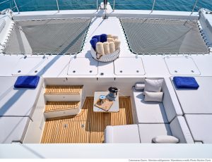Pokład katamaranu Sunreef Yachts z obszarem wypoczynkowym wyposażonym w wygodne poduszki i schody prowadzące na dolny pokład, wszystko pod bezchmurnym niebieskim niebem.