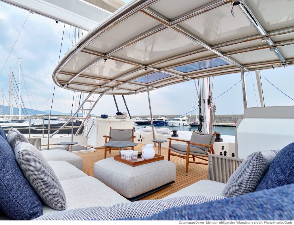 Pokład katamaranu Sunreef Yachts z wygodnymi siedzeniami z widokiem na marinę z innymi jachtami w tle.