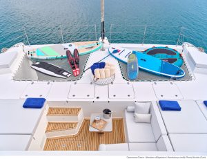 Dziób luksusowego katamaranu Sunreef Yachts z miejscem do wypoczynku, siedzeniami i zestawem sprzętu do sportów wodnych na siatce, w tym deski paddleboard.