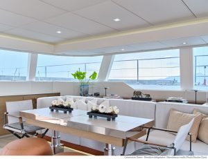 Wnętrze luksusowego katamaranu Sunreef Yachts z eleganckim salonem z dużym białym stołem, kremowymi sofami i panoramicznymi oknami zapewniającymi obfite naturalne światło.