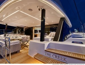 Luksusowy pokład katamaranu Sunreef Yachts o nazwie 'THE CREEK' o zmierzchu, z eleganckimi meblami, oświetleniem i drewnianą podłogą.