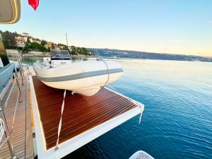 Jacht marki Sunreef Yachts zacumowany nad wodą podczas zachodu słońca, z pontonem na tylnej pokładzie i malowniczą linią brzegową w tle.