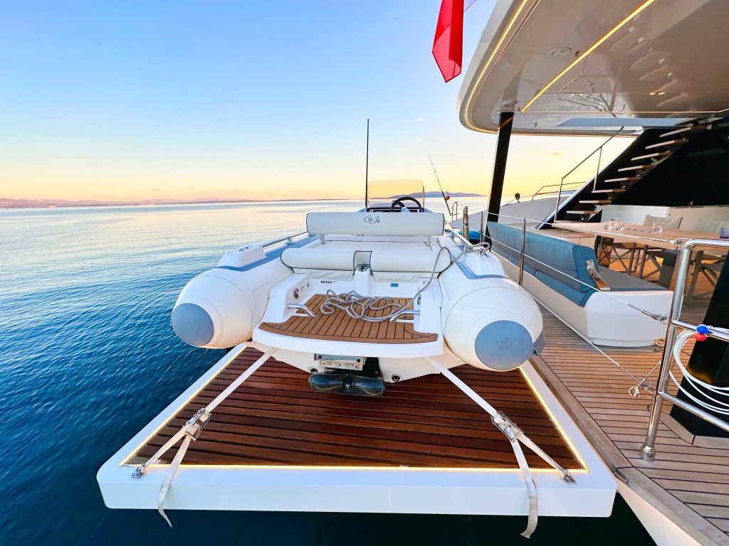 Łódź pneumatyczna zawieszona na rufie luksusowego katamaranu Sunreef Yachts z oceanem i zachodem słońca w tle.