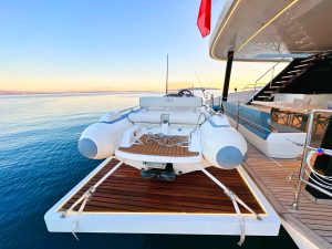 Łódź pneumatyczna zawieszona na rufie luksusowego katamaranu Sunreef Yachts z oceanem i zachodem słońca w tle.