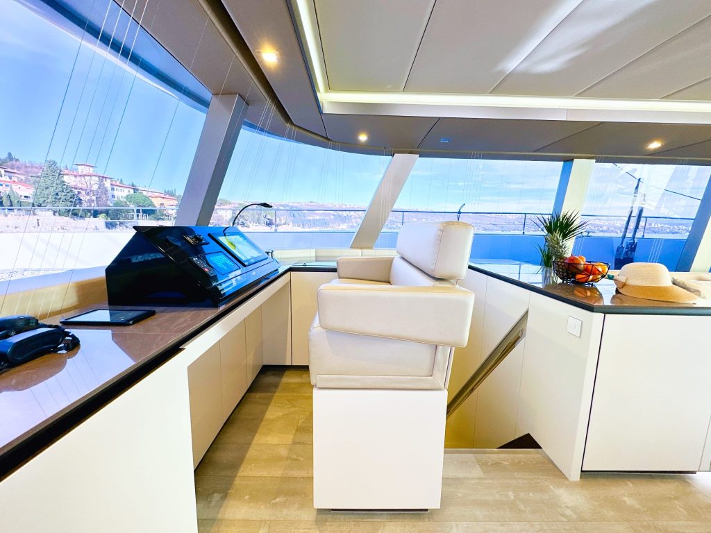 Wnętrze luksusowego katamaranu Sunreef Yachts z nowoczesnym stanowiskiem sterowania, dużym białym fotelem kapitańskim i panoramicznymi oknami.