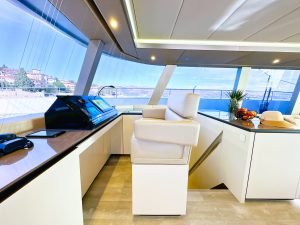 Wnętrze luksusowego katamaranu Sunreef Yachts z nowoczesnym stanowiskiem sterowania, dużym białym fotelem kapitańskim i panoramicznymi oknami.
