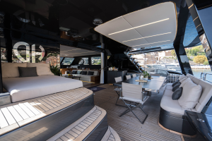 The image shows the luxurious deck of a Sunreef Yachts catamaran, featuring an elegant dining area with chairs and table, surrounded by comfortable seating. Large windows offer a view of the water and distant yachts.
