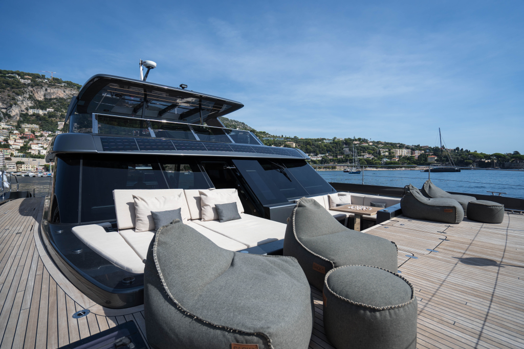 A luxurious Sunreef Yachts catamaran with a spacious deck featuring modern seating and sunbathing areas, set against a backdrop of a scenic coastal town.