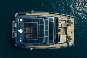 A top view of a luxury Sunreef Yachts catamaran on clear blue water, featuring solar panels on the roof and an elegant deck with seating arrangements.