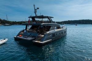 A luxurious Sunreef Yachts catamaran anchored in a calm bay with hills in the background, surrounded by other boats on a sunny day.