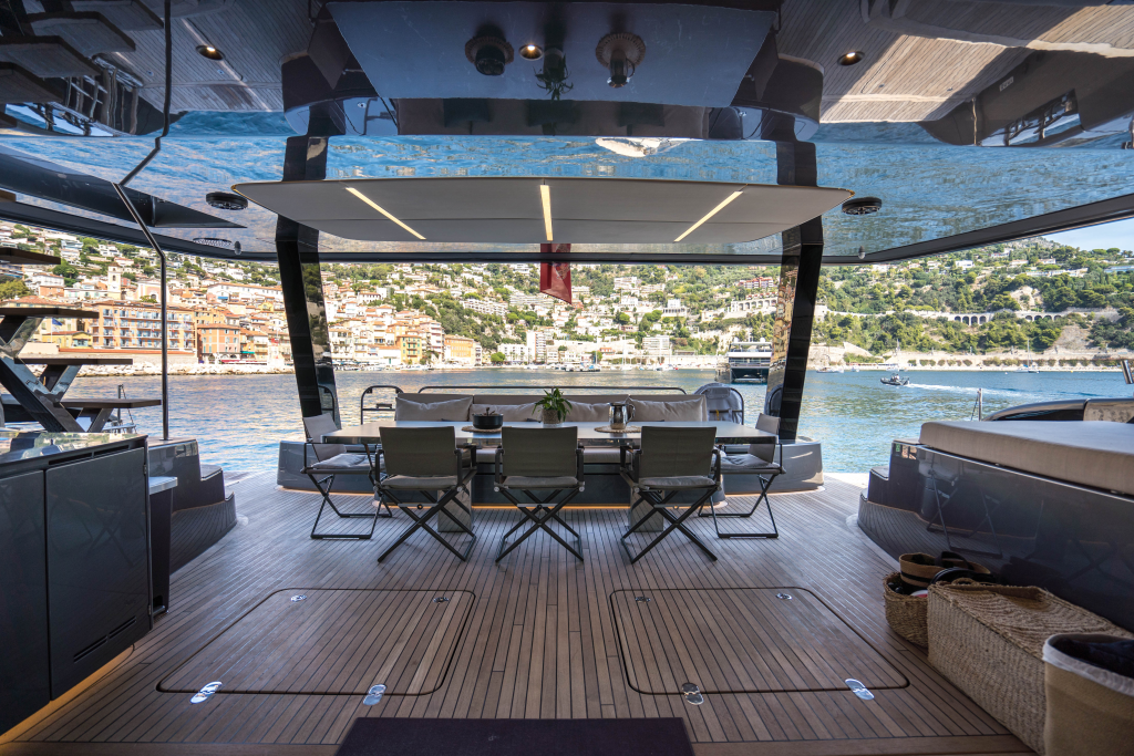 The Sunreef Yachts deck features a spacious outdoor seating area with folding chairs, overlooking a scenic waterfront town on a sunny day.