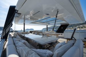 A luxurious yacht deck by Sunreef Yachts features comfortable seating, a large table, and a hammock. The view overlooks a serene harbor with sailboats and a distant coastline.