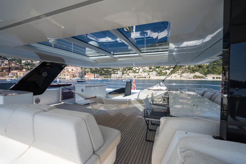 The image shows a luxurious deck of a Sunreef Yachts catamaran. It features comfortable seating, a hammock, and views of a coastline with buildings in the background.