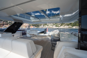 The image shows a luxurious deck of a Sunreef Yachts catamaran. It features comfortable seating, a hammock, and views of a coastline with buildings in the background.