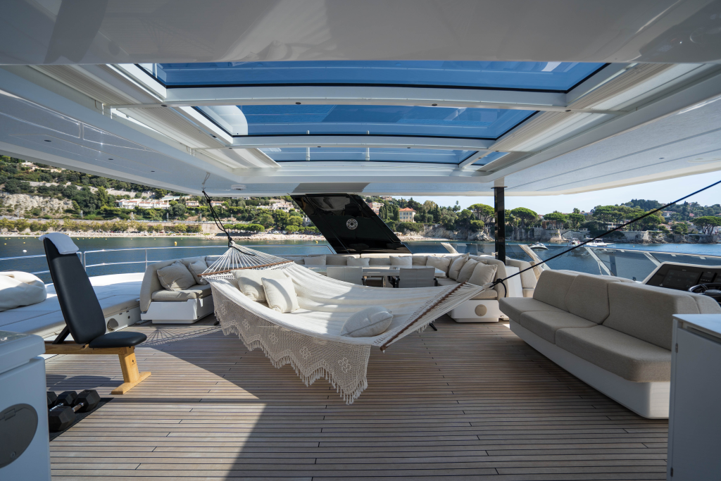 The deck of a luxury yacht by Sunreef Yachts features a hammock, lounge chairs, and sofas, with a scenic view of the coastline.