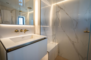 A luxurious bathroom interior on a Sunreef Yachts vessel, featuring a sleek white sink with modern fixtures, marble-style walls, and a glass shower enclosure.