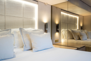 A luxurious bedroom on a Sunreef Yachts vessel featuring plush white bedding, soft pillows, and ambient lighting, with a mirrored wall reflecting the elegant design.