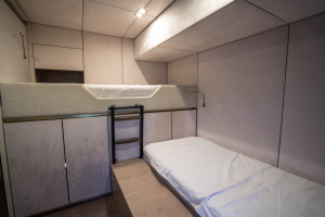 The interior of a Sunreef Yachts cabin features a bunk bed setup, with a ladder leading to the top bed. The room is modern and compact, with minimalistic design and soft lighting.