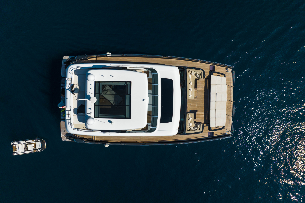 An aerial view of a luxurious Sunreef Yachts catamaran with three decks visible, anchored on calm blue water, alongside a small motorboat on the left side.