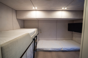 The photo showcases a Sunreef Yachts interior cabin featuring a bunk bed setup. The top and floor-level beds both have white bedding. The walls are a muted beige, and there is a small black screen or panel on the right wall.