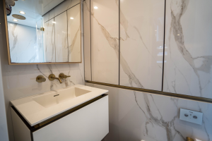 The image shows a luxurious bathroom interior on a Sunreef Yachts vessel, featuring a modern sink with a marble backsplash, sleek fixtures, and a mirrored cabinet.