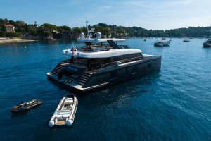 A luxury yacht named Sunreef Yachts is anchored in a scenic bay surrounded by several boats. The yacht has a modern design with a spacious deck.