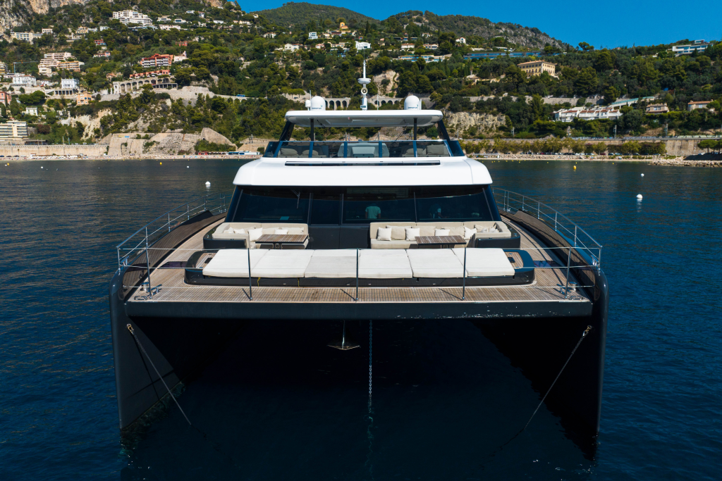 The image shows a Sunreef Yachts luxury catamaran on the water with a backdrop of coastal hills and houses.