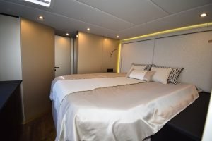 Luksusowa sypialnia na katamaranie Sunreef Yachts z dużym łóżkiem z białą i beżową pościelą, otoczona eleganckim oświetleniem i nowoczesnym wystrojem.
