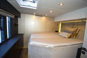 Interior scene of a luxurious Sunreef 50 Welcome Back cabin, featuring a large bed with elegant bedding and a hat placed on it. The room has modern furnishings and ambient lighting.