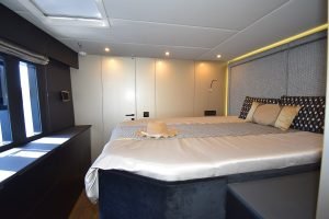 Wnętrze luksusowej kabiny jachtu Sunreef Yachts, z dużym łóżkiem z elegancką pościelą i kapeluszem na nim. Pomieszczenie posiada nowoczesne wyposażenie i nastrojowe oświetlenie.
