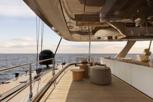 Pokład luksusowego katamaranu Sunreef Yachts z drewnianą podłogą i stylowymi meblami, z widokiem na spokojne morze pod częściowo zachmurzonym niebem.
