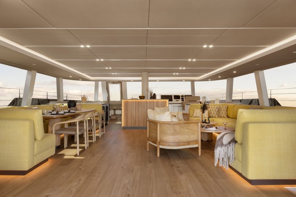 Wnętrze luksusowego katamaranu Sunreef Yachts z eleganckimi żółtymi siedziskami, jadalnią i panoramicznymi oknami z widokiem na ocean.