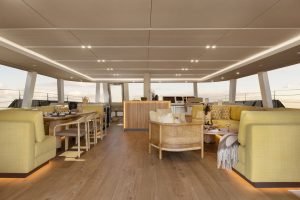 Wnętrze luksusowego katamaranu Sunreef Yachts z eleganckimi żółtymi siedziskami, jadalnią i panoramicznymi oknami z widokiem na ocean.