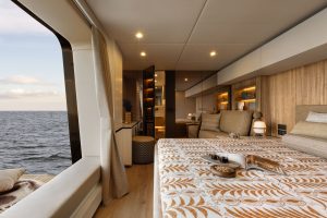 Wnętrze pokoju Sunreef Yachts z widokiem na morze, z przytulnym łóżkiem z wzorzystym kocem, ozdobną lampą i dużymi oknami zapewniającymi malowniczy widok na ocean.