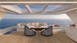 The image shows a luxurious yacht deck, possibly from Sunreef Yachts, featuring cushioned seating, a table with decorative items, and a panoramic sea view through large windows.