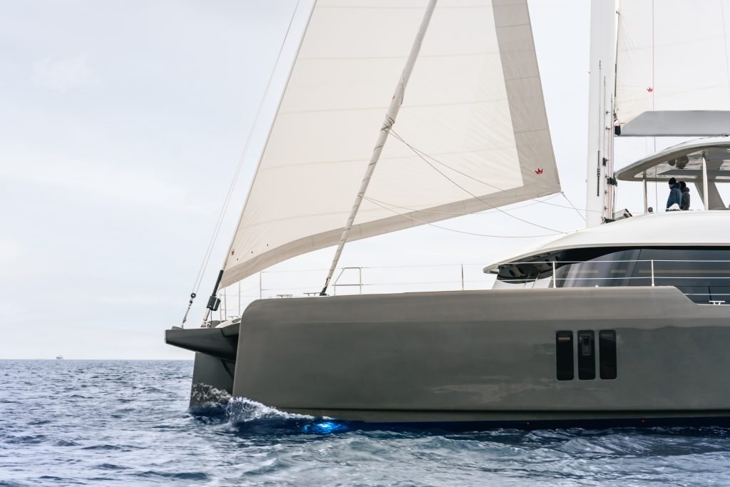 A Sunreef Yachts catamaran sailing on the open sea with its white sails unfurled under a cloudy sky.