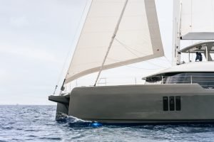 A Sunreef Yachts catamaran sailing on the open sea with its white sails unfurled under a cloudy sky.