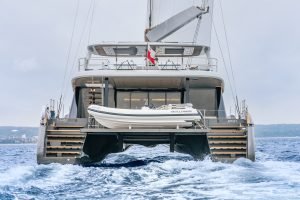A Sunreef Yachts catamaran is sailing on the ocean, showing its rear design with an additional small boat named Williams. The name Candy is visible on the side.