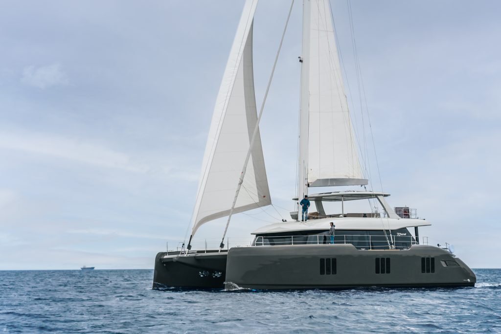 A luxury Sunreef Yachts catamaran sailing on the open sea with white sails against a cloudy sky.