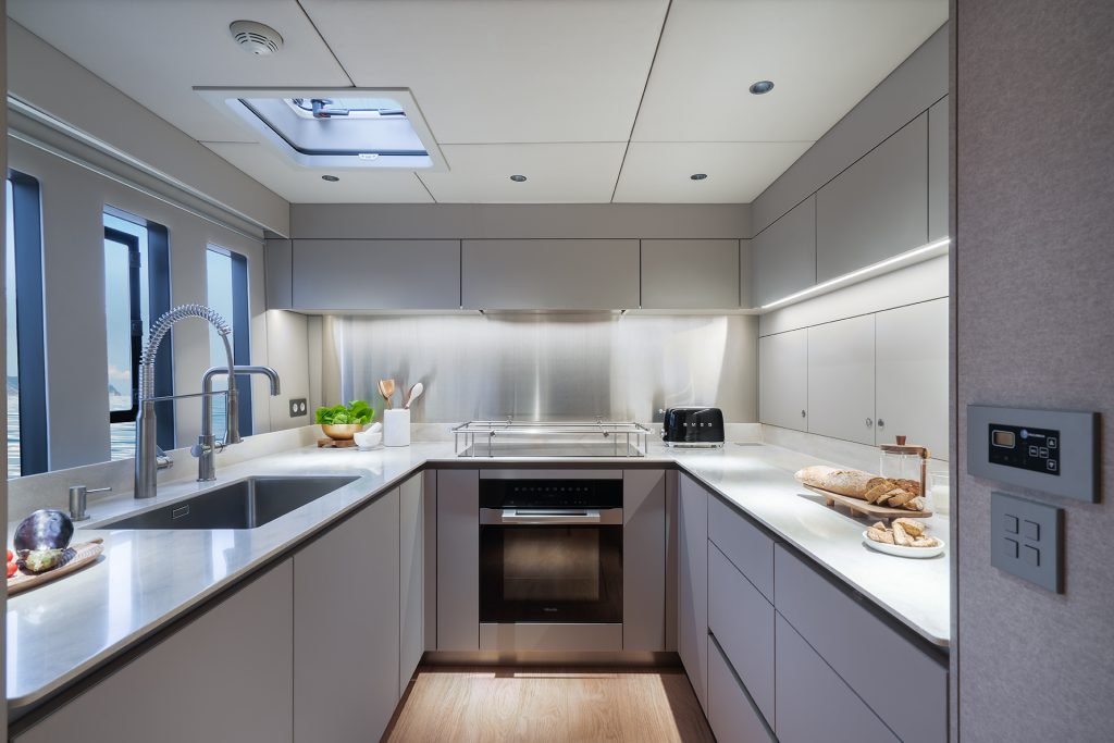 Interior of a Sunreef Yachts kitchen with modern white cabinets, a sleek design, and stainless steel appliances. Natural light filters through a skylight above.