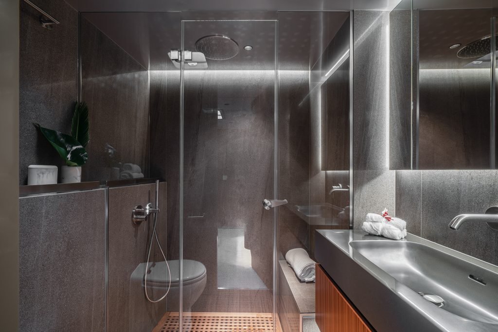 A modern bathroom inside a Sunreef Yachts vessel featuring sleek grey walls, a glass-enclosed shower, a minimalist sink with a mirror, and wooden accents.