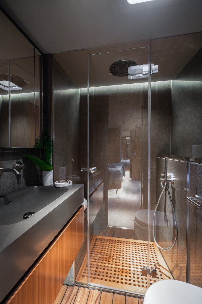 A luxurious bathroom aboard a Sunreef Yachts vessel. The space features a modern design with a glass-enclosed shower, wooden flooring, and sleek black countertops. A small potted plant adds a touch of greenery.