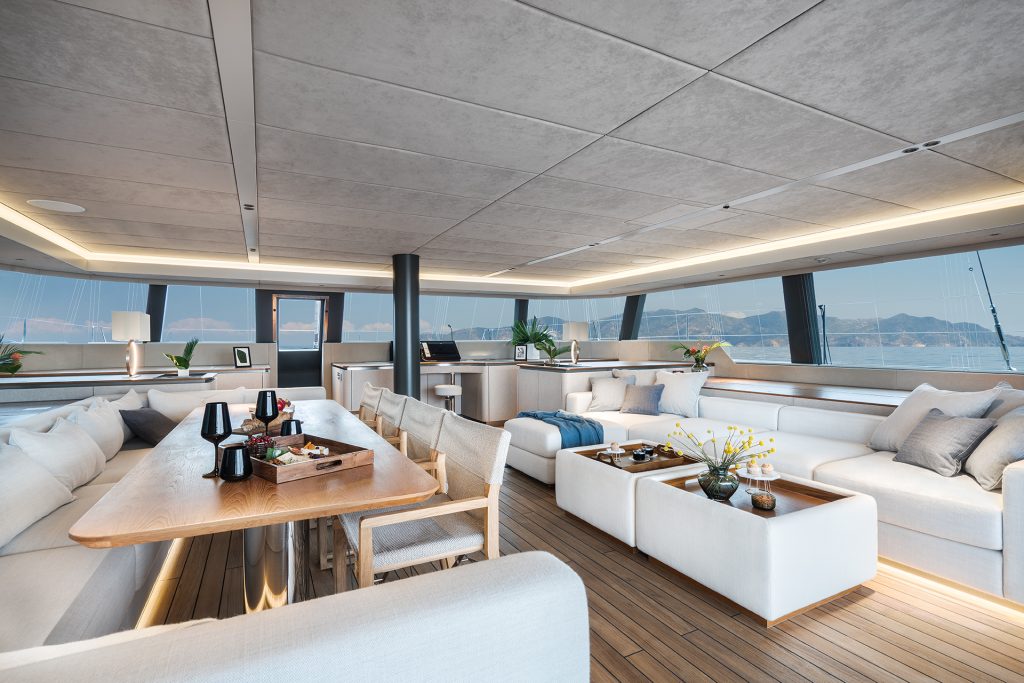 The luxurious interior of a Sunreef Yachts catamaran features spacious seating areas with white sofas, a wooden dining table, and modern decor under a large windowed ceiling.