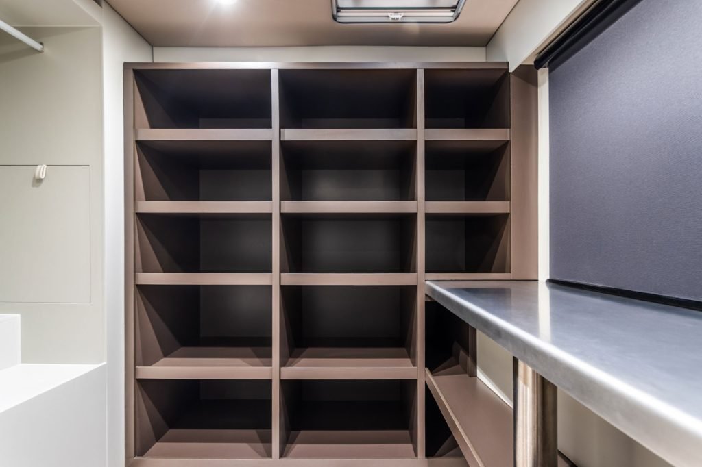The image shows an organized storage area inside a Sunreef Yachts vessel, featuring a large shelving unit with multiple square compartments against a wall, and a metal countertop on the right.