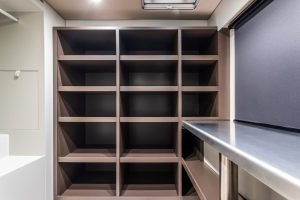 The image shows an organized storage area inside a Sunreef Yachts vessel, featuring a large shelving unit with multiple square compartments against a wall, and a metal countertop on the right.